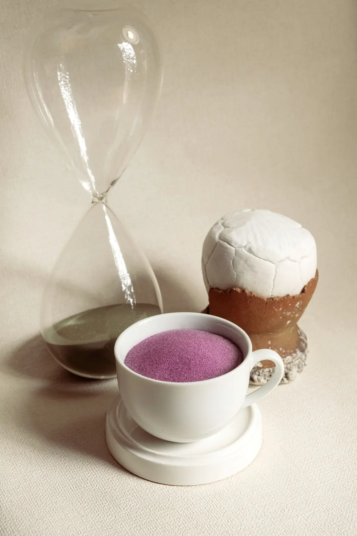 Fine Philippine ube powder in a white cup beside an hourglass, an editorial still life of Dioscorea alata purple yam powder
